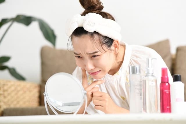鏡の前で毛穴やたるみに悩む女性